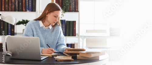 Young woman studying at a desk with a laptop and books, focused on learning a...