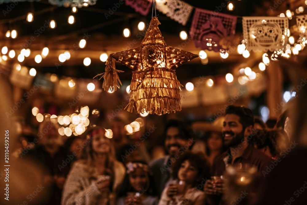 Obraz premium A golden star pinata hangs above a joyful crowd during a festive Mexican posada, featuring warm incandescent lights and papel picado for traditional holiday celebration visuals