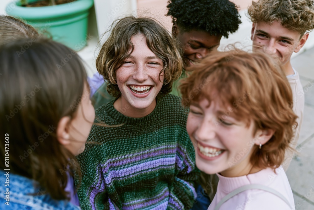 Fototapeta premium Group of diverse young friends laughing and chatting on a city street, wearing cozy knit sweaters in a joyful community and youth lifestyle moment