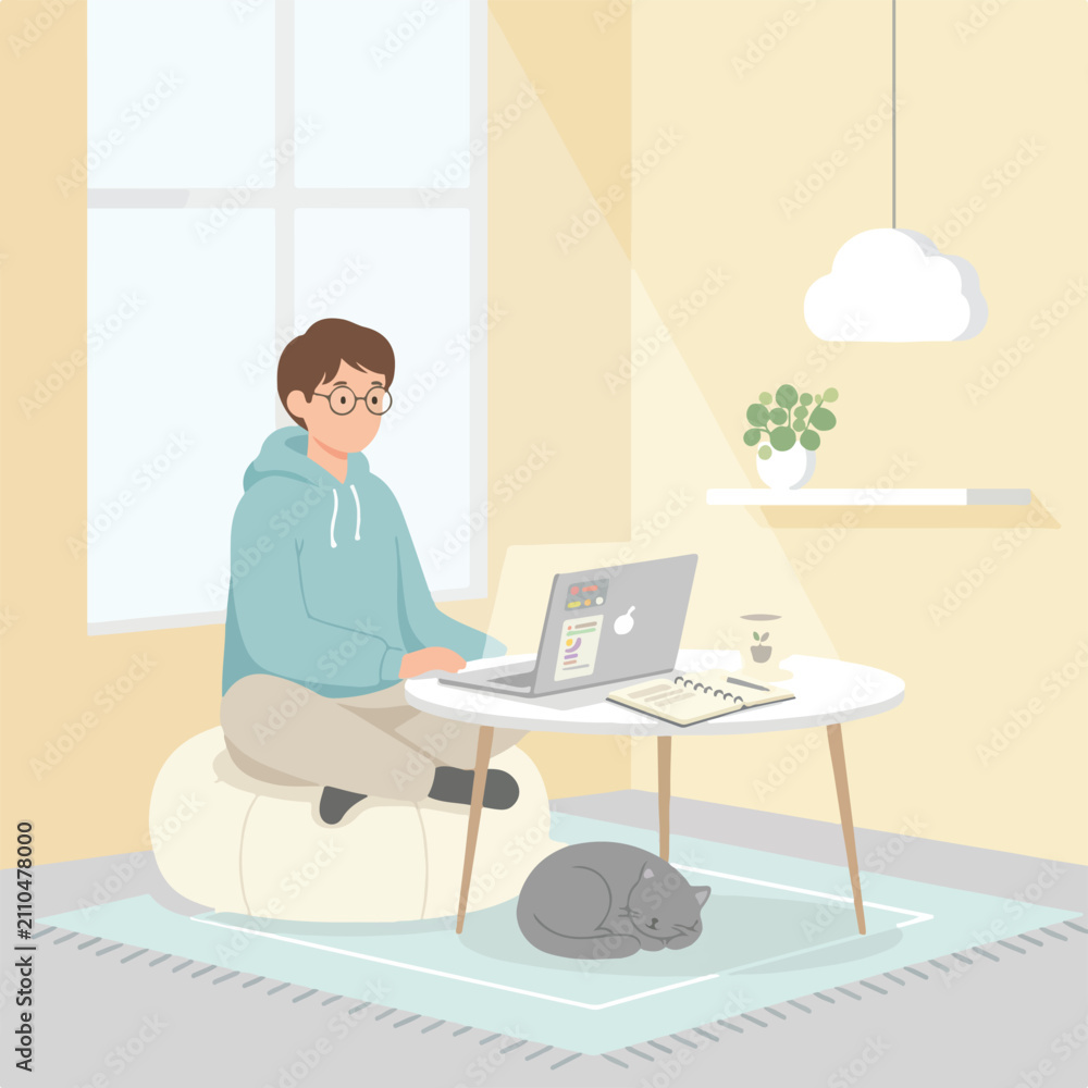 Fototapeta premium A man wearing glasses sits on a bean bag chair while working on his laptop at a low table in a cozy room with his sleeping cat nearby.
