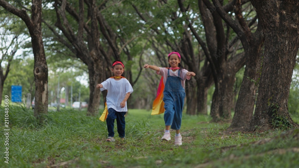 Fototapeta premium Active Asian little kids pretending to be superheroes playing together outdoors in nature park. Children roleplay, imaginative fantasy, and brave hero childhood lifestyle.