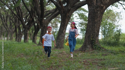 Foto Cute Asian children wearing superhero cape and mask having fun running in tree tunnel park
