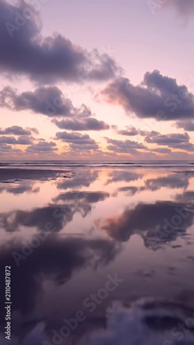 Ocean waves reflecting purple sunset sky on sandy beach.