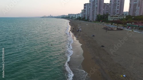Mersin, Turkey. Low aerial flight over the wave surge line along Mezitli beach, with first-line apartment towers and people relaxing at the water's edge. Aerial View