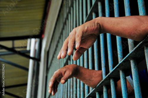 Bild auf Leinwand Close-up of a prisoner's hands gripping the iron bars of a jail cell