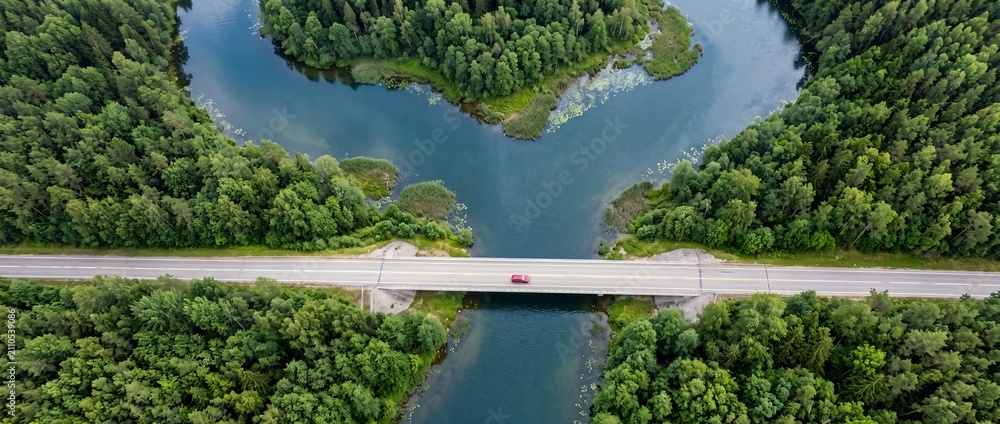 Obraz premium Aerial view of a road bridge over a river flowing through a dense green forest
