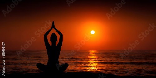 Silhouette of a person meditating by the ocean at sunset.