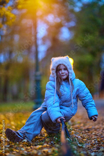 Child plays in park during autumn while holding a stick and wearing a warm coat