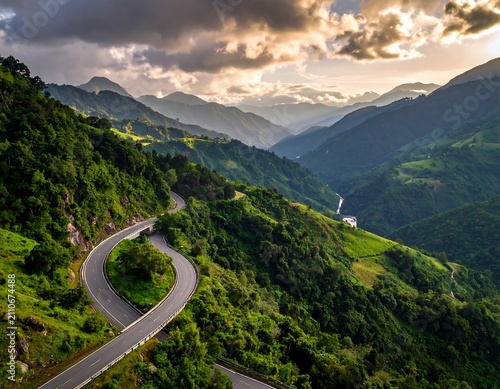 Aerial view of a winding road snaking through verdant, mountainous terrain, illuminated by golden sunlight breaking through cloudy skies