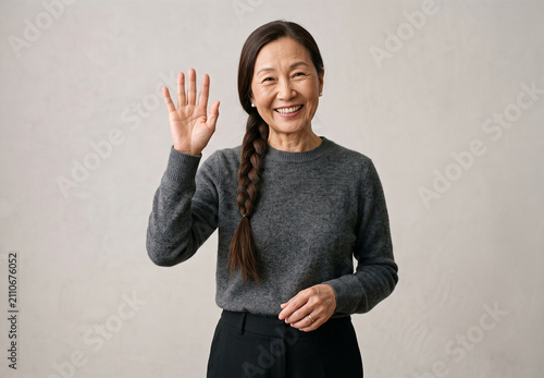 Portrait of friendly senior Asian woman waving hand saying hello with warm smile