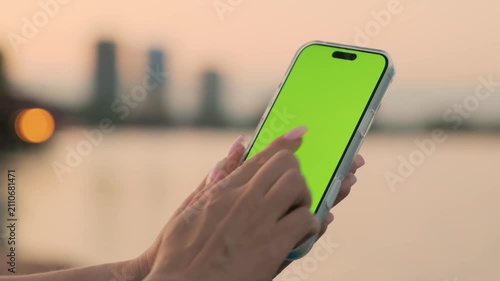 Woman Using Smartphone with Vertical Green Screen Chroma Key Against of River on City Waterfront