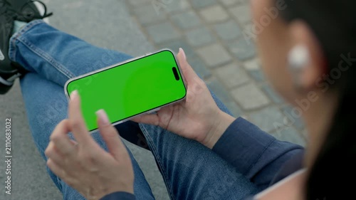 Woman Using Smartphone with Green Screen Mock-up and Headphones On City Park