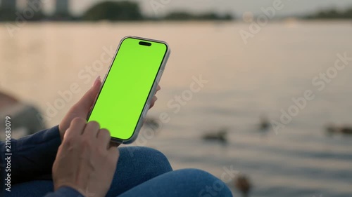 Woman Using Smartphone with Vertical Green Screen Chroma Key Against of River on City Waterfront