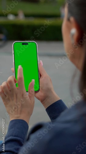 Woman Using Smartphone with Green Screen Mock-up and Headphones On City Park. Vertical Video