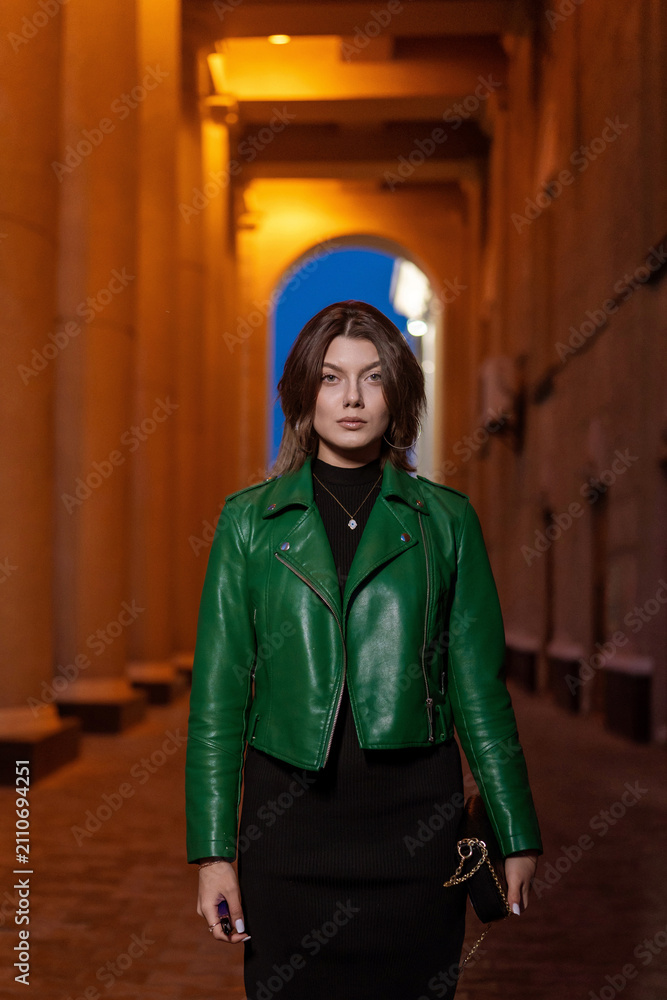Obraz premium Stylish woman in green leather jacket posing in city night