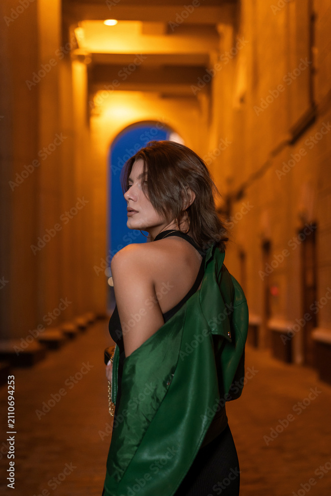 Obraz premium Stylish woman in green leather jacket posing in city night