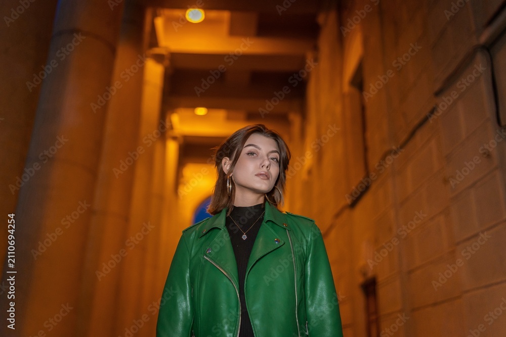 Obraz premium Stylish woman in green leather jacket posing in city night