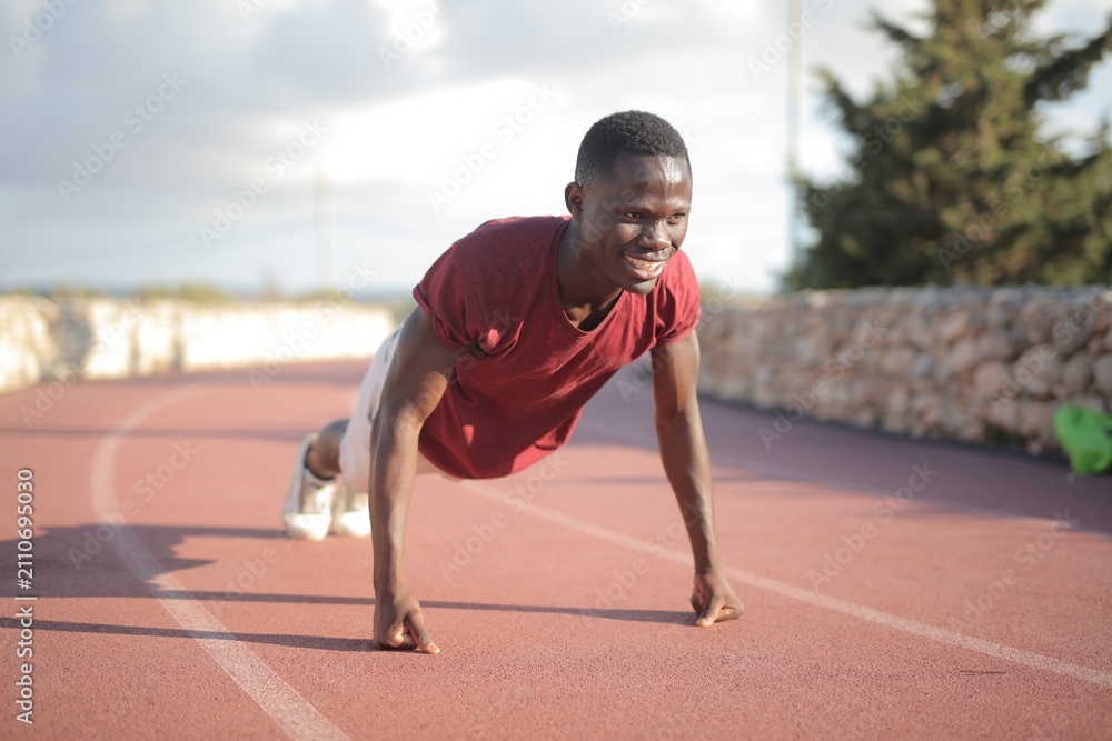 Fototapeta premium Young Black man smiling while doing pushups outdoors