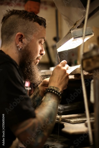 Tattooed artisan making custom jewelry at his workbench