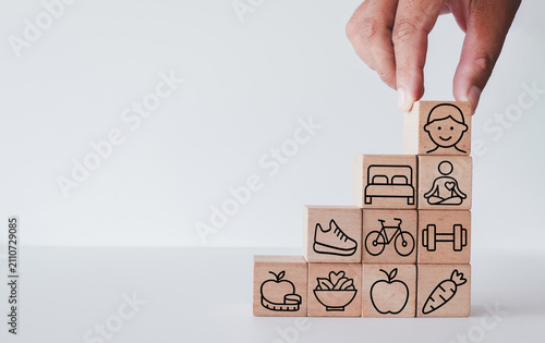 Healthy lifestyle and well-being concept. Hand stacking wooden blocks with happy face, fitness, sleep, and diet icons like stairs. Building holistic health and physical balance.