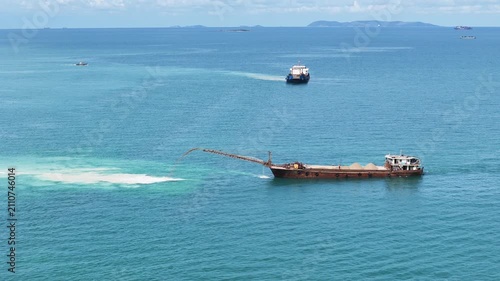 Sand dredging ship discharging sand into the sea for land reclamation project. Coastal engineering and marine infrastructure development. Industrial vessel working on artificial island construction.