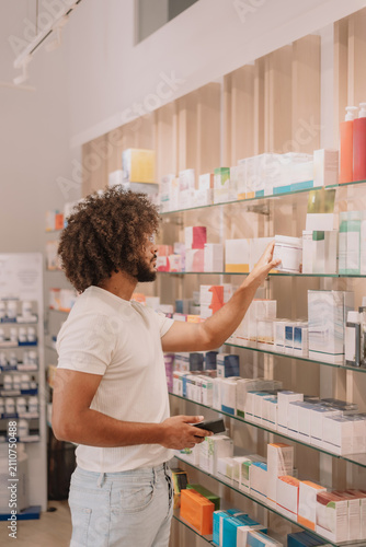 African American man choosing product from shelf while shopping in pharmacy store