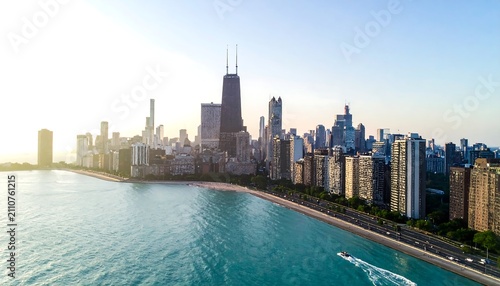 Aerial view of a city skyline at sunset, with tall buildings against the fading sun along a blue lake and a boat