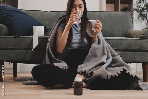 Photos sick asian young woman sneezing into tissue paper while covered with a blanket a