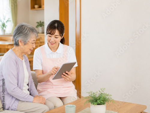 Japanese caregiver showing digital care records to a senior woman during a friendly home care consultation