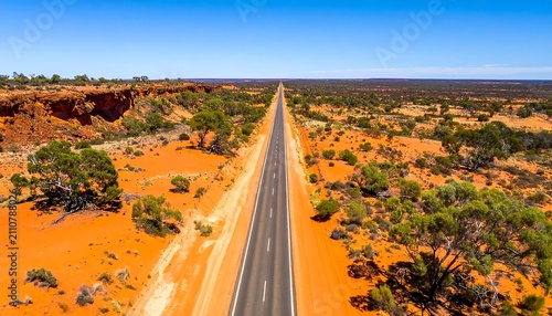 Aerial view of a straight asphalt road cutting through vast, arid landscape under a clear blue sky