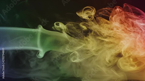 Colorful abstract smoke swirling with green yellow and red hues on dark background