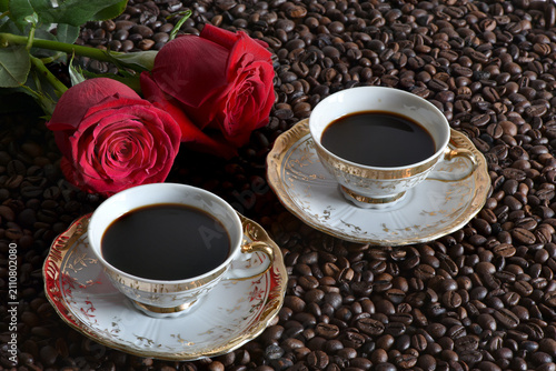 pair of coffee cups with a red rose nearby, coffee beans in the background