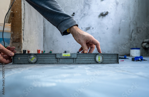 Worker carefully leveling newly laid tiles on a bathroom floor during house renovation, ensuring a perfect and precise installation process with construction tools