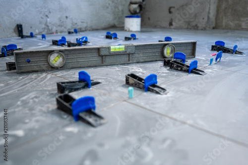 Tiler installing new ceramic floor tiles with a tile leveling system, ensuring even surfaces for house renovation work on a construction site