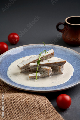 Sliced breaded tofu sticks in creamy white sauce on a blue plate decorated with microgreens, dark grey background.