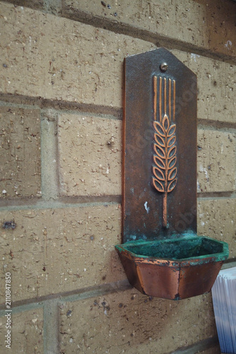 Fotografie Aged copper holy water font with wheat symbol and green patina fixed on a rustic brick wall