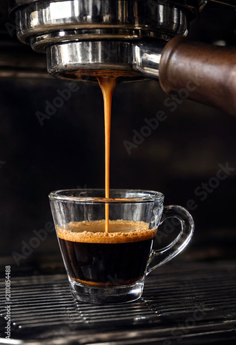 Closeup of freshly brewed espresso coffee pouring into a clear glass cup from machine