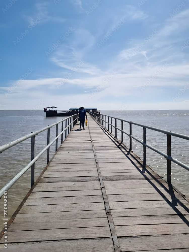 Fototapeta premium Long wooden pier extending into calm ocean waters. Scenic coastal walkway with metal railings for safety and leisure strolls.