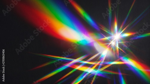 Vibrant rainbow light beams radiating from a bright white starburst on a dark background with beams emanating central against dark backdrop colorful light multicolor prismatic abstract