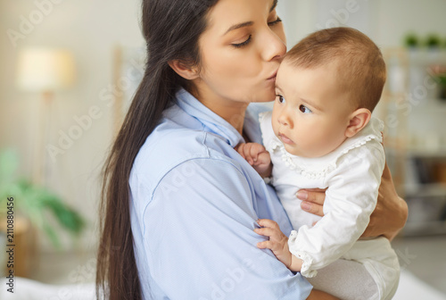 Принти на полотні Mother holds baby in bright home, sharing tender kiss and affectionate moment that reflects warmth and warm maternal