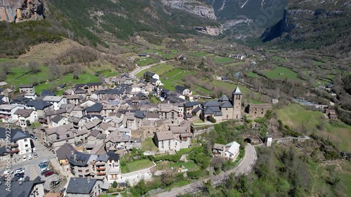 Orbital aerial shot of Torla-Ordesa village and covered with snow mountains of Ordesa y Monte Perdido National Park on sunny spring day. Huesca, Spain.