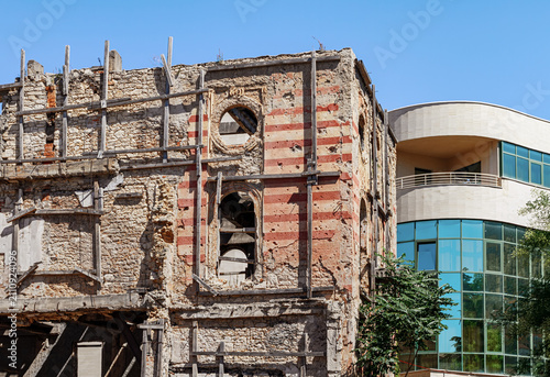 Foto A weathered stone facade with visible war damage contrasts with a modern building beneath a clear blue sky in Mostar