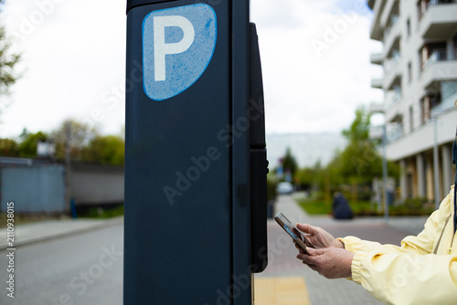 Close up view of a person making a modern contactless payment with a smartphone at an outdoor self-service parking meter. The shot highlights wireless NFC technology, digital banking, urban automation