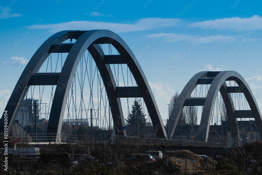 Fototapeta premium Modern steel arch bridge with suspension cables over an urban construction area