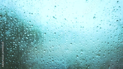 The scene shows water droplets on a glass pane, with rain creating a misty view. Rain blurs the outside landscape, enhancing the rainy atmosphere.