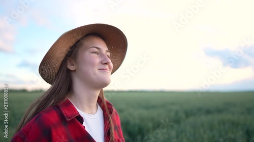 The woman in a straw hat smiles contentedly in a green field. The woman wears a red plaid shirt, enjoying the tranquility of the rural landscape.