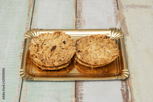 Two almond florentine cookies on a shiny gold tray over a distressed wooden background.