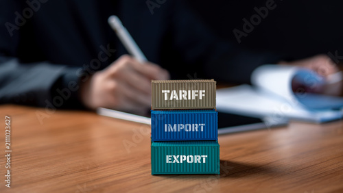 Tariff import export trade war and customs duty policy concept. Miniature cargo containers with tariff import and export text on wooden desk while businessman signs trade documents.