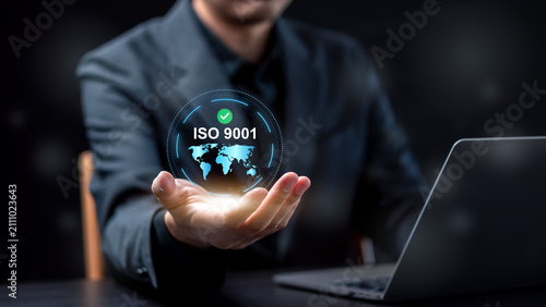 ISO 9001 international quality management certification standard concept. Businessman holding virtual globe hologram with ISO 9001 text and green checkmark over laptop.