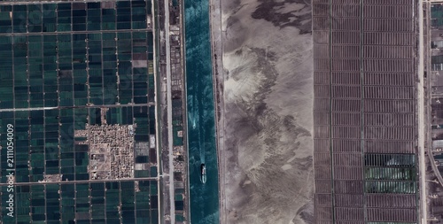 Obraz na plátně Aerial view of a checkerboard of aquaculture ponds beside the Suez Canal near Ismailia Egypt where two ships travel past a bordering desert strip